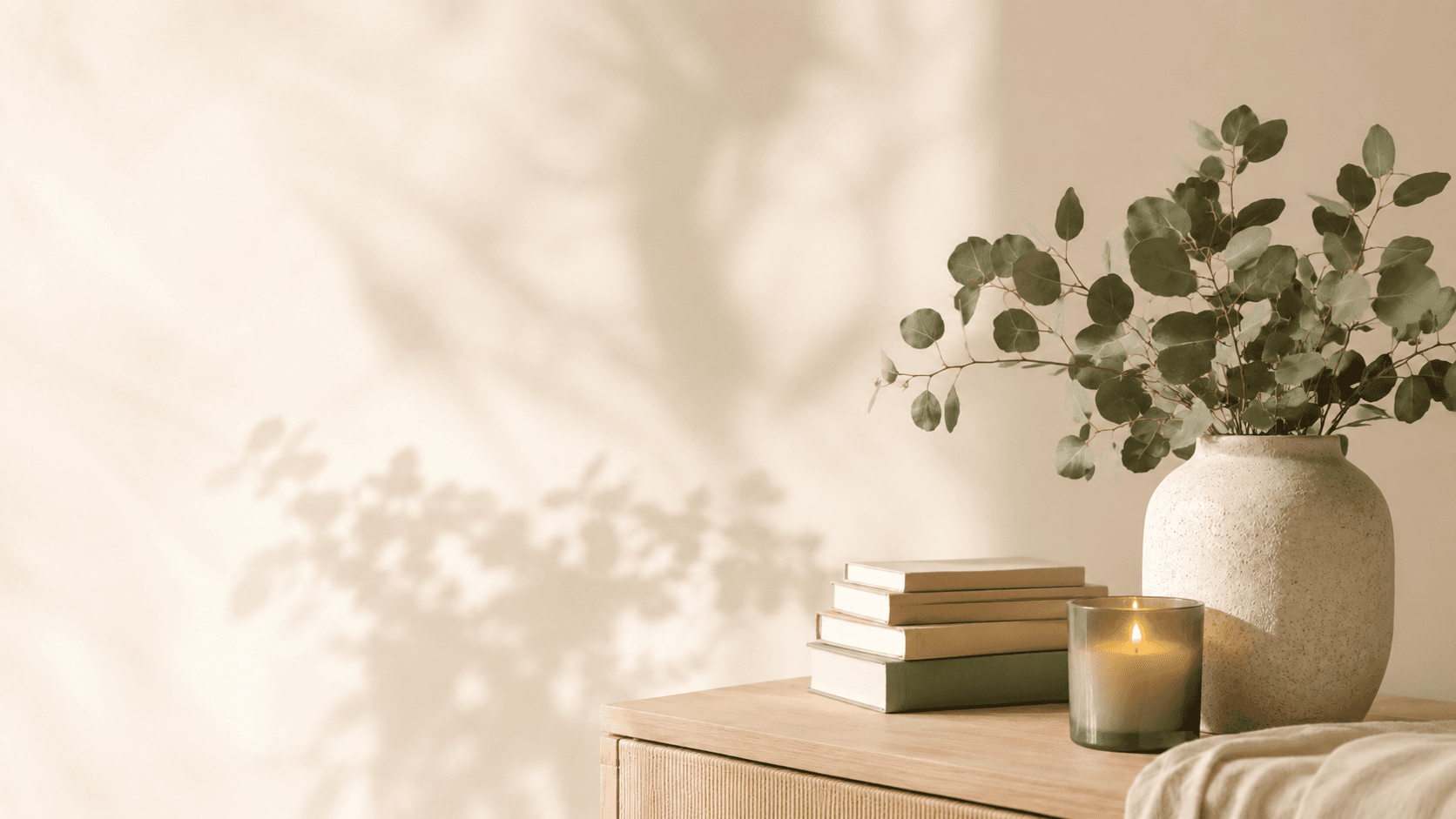 Eucalyptus in a ceramic vase beside a candle and books in a calm, sunlit room